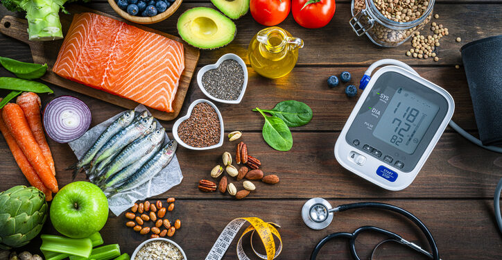 Healthy food for heart care: overhead view of healthy food rich in Omega-3 and antioxidants and a blood pressure monitor, tape measure and stethoscope shot on wooden table. The composition includes a salmon fillet, sardines, avocado, extra virgin olive oil, brown lentils, celery, artichoke blueberries, celery, carrots, brown lentils, asparagus, artichoke, broccoli, flax seeds, chia seeds and some nuts like almonds, pistachio and pecan. High resolution 42Mp studio digital capture taken with SONY A7rII and Zeiss Batis 40mm F2.0 CF lens